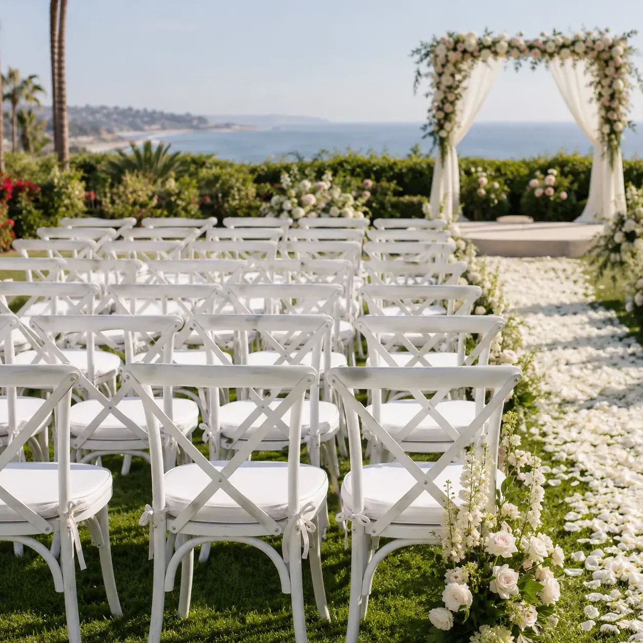 Elegant ceremony chair setup in Orange County, California, with white chairs, floral aisle decor, wedding arch, and coastal outdoor view.