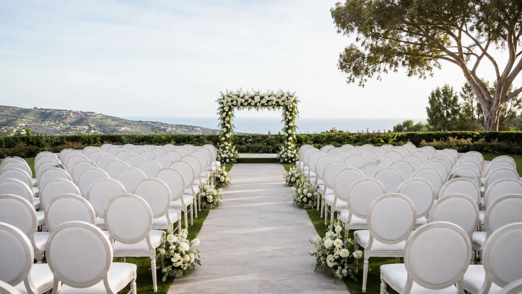 Outdoor ceremony chair setup in Orange County, California, with white chairs, floral aisle decor, wedding arch, and ocean view.